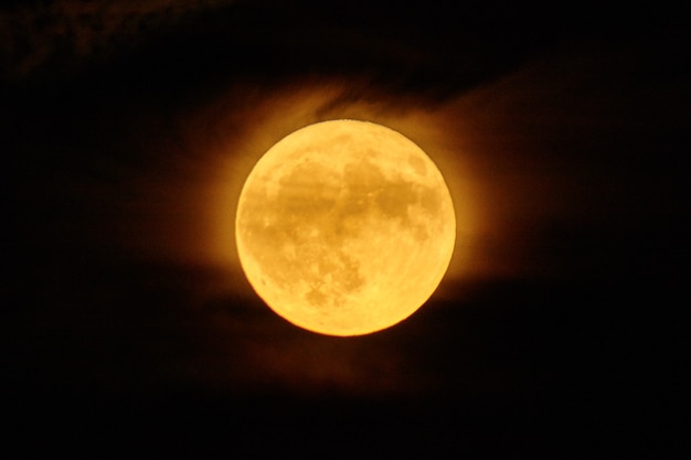 Photo image de la pleine lune qui est une lune de récolte orange brillant avec une couverture nuageuse brumeuse