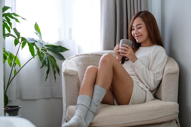 Image de portrait d'une belle femme asiatique buvant du café chaud et se relaxant sur un canapé dans la chambre à la maison