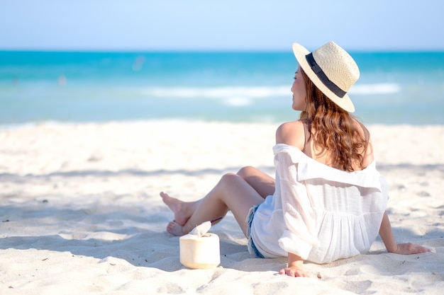 Image portrait d'une belle femme asiatique s'asseoir et boire du jus de noix de coco sur la plage