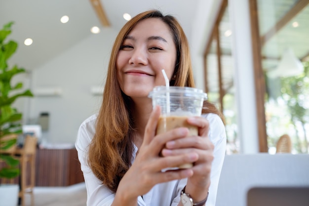 Image de portrait d'une belle jeune femme asiatique tenant et buvant du café glacé au café