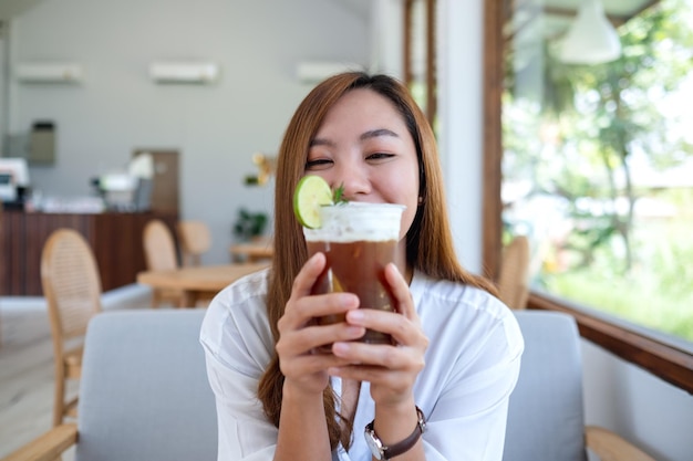 Image de portrait d'une belle jeune femme asiatique tenant et buvant du café glacé