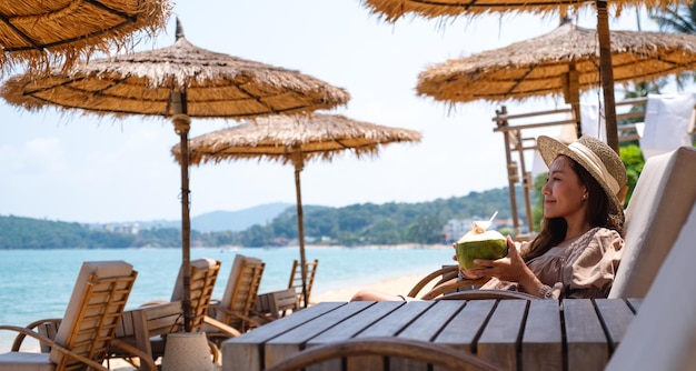 Image de portrait d'une belle jeune femme asiatique tenant et buvant du jus de noix de coco sur la plage