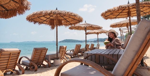 Image de portrait d'une belle jeune femme asiatique tenant et buvant du jus de noix de coco sur la plage