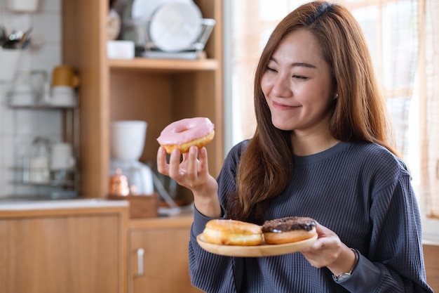 Image de portrait d'une belle jeune femme asiatique tenant et mangeant un beignet à la maison