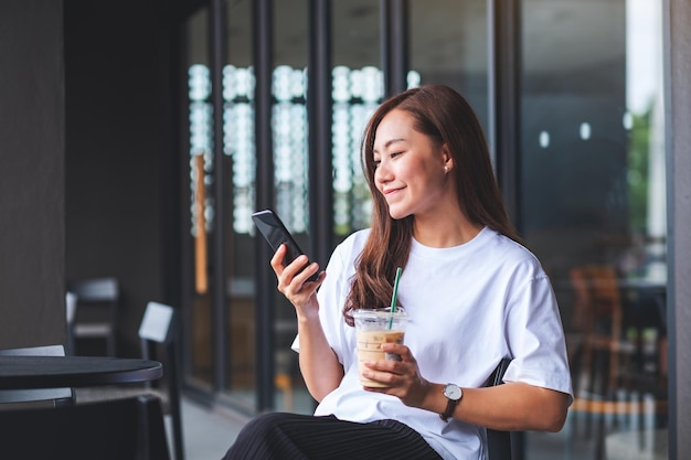 Image de portrait d'une belle jeune femme asiatique tenant et utilisant un téléphone portable tout en buvant du café au café