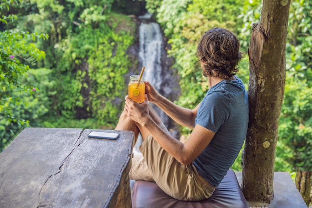 Image de portrait en gros plan d'un bel homme buvant du thé glacé avec un sentiment de bonheur dans la nature verdoyante et le fond du jardin en cascade