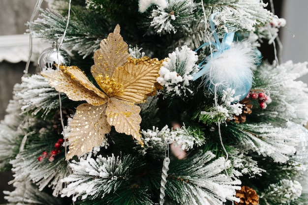 Image de près d'un arbre de Noël artificiel décoré de boules et de cônes avec des extrémités blanchies. Étoile feuille d'or sur une branche.