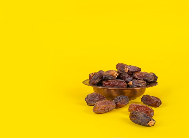 Image rapprochée d'un bol de cuivre, de dattes sèches, de fruits, d'un espace de copie de fond de studio jaune, prêt à manger.