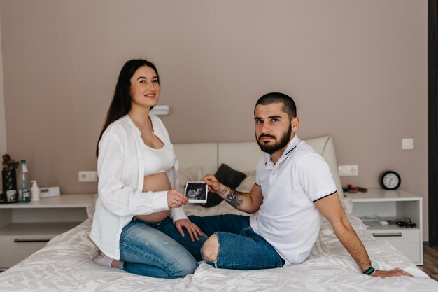 Image recadrée de la belle femme enceinte et son beau mari tenant une échographie