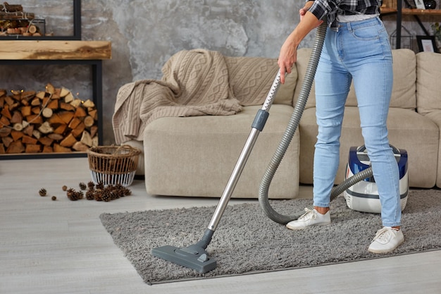 Image recadrée d'une belle jeune femme utilisant un aspirateur tout en nettoyant un tapis dans la maison