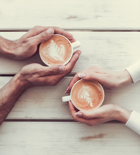 Image recadrée de couple amoureux tenant des tasses de café.