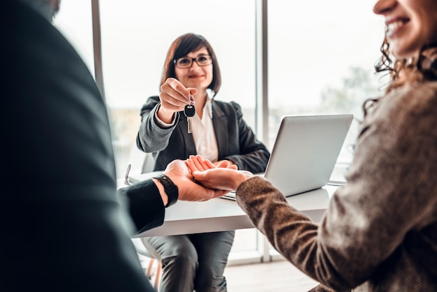 Image recadrée d'un couple familial heureux faisant l'achat de la première maison en prenant la clé d'un agent immobilier féminin