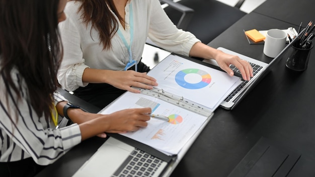 Image recadrée de deux femmes d'affaires prospères et intelligentes dans une équipe financière travaillant et analysant ensemble les données de l'entreprise.