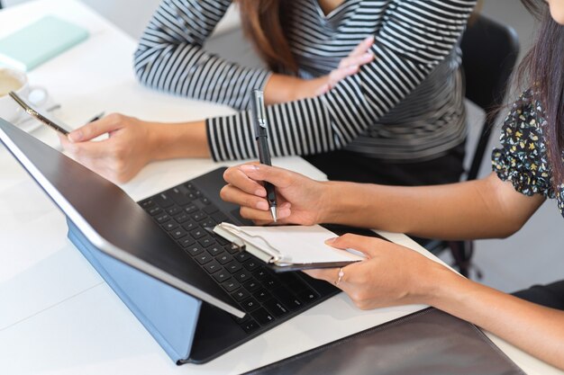 Image recadrée de deux femmes dans des looks décontractés discuter et énumérer une idée d'entreprise pour une tablette de travail sur le bureau