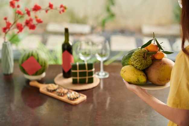 Image recadrée d'une femme apportant une assiette de fruits frais à la table du dîner