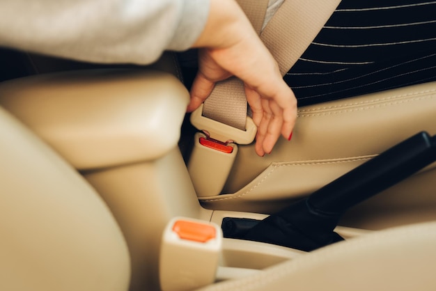 Image recadrée d'une femme assise dans une voiture et mettant sa ceinture de sécurité