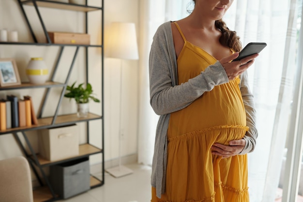 Image recadrée sur une femme enceinte prenant rendez-vous chez le médecin via une application sur smartphone