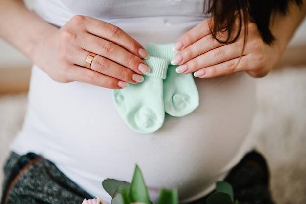 Image recadrée femme enceinte tenant des chaussettes pour un bébé sur son ventre. Enceinte étreignant le ventre à la maison. Notion de maternité. Douche de bébé.