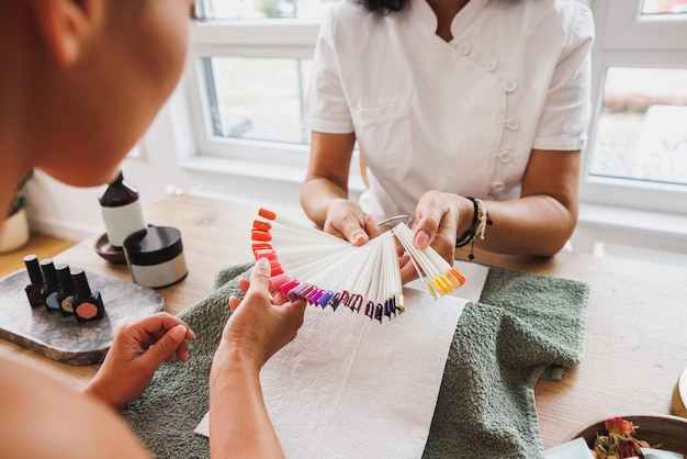 Photo l'image recadrée d'une femme est assise devant une esthéticienne et choisit la couleur des ongles pendant le traitement de manucure.