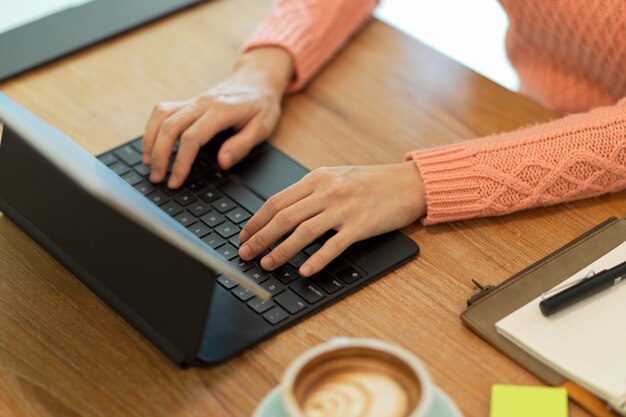 Image recadrée d'une femme en pull rose tapant sur un clavier travaillant sur une tablette portable