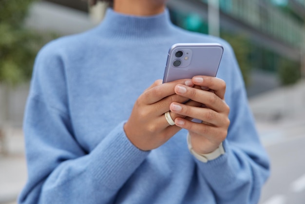 L'image recadrée d'une femme sans visage méconnaissable en pull bleu décontracté contient des types de téléphones portables sms