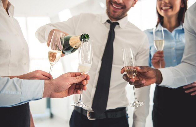 Image recadrée de gens d'affaires prospères buvant du champagne parlant et souriant tout en célébrant au bureau