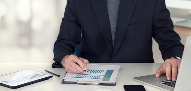 Image recadrée d'un homme d'affaires utilisant un ordinateur portable et analysant un graphique, assis au bureau, planification et stratégie d'entreprise.