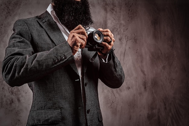 Image recadrée d'un homme barbu portant un costume formel tenant un appareil photo. Isolé sur un fond texturé gris.