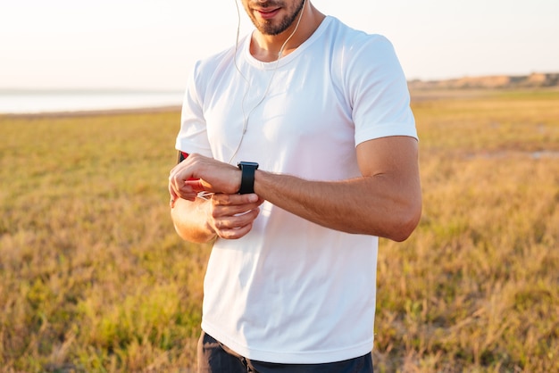 Image recadrée d'un homme sportif regardant sa smartwatch avec des écouteurs