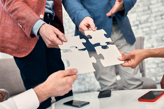 Image recadrée d'hommes d'affaires joignant les pièces du puzzle au bureau