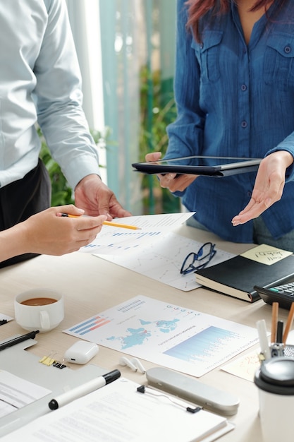 Image recadrée d'hommes d'affaires vérifiant divers graphiques et rapports lors d'une réunion et discutant des dépenses d'entreprise