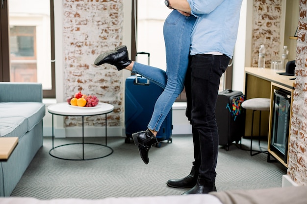 Image recadrée de jambes de jeune couple d'amoureux dans des vêtements décontractés, passer du temps romantique ensemble, étreindre dans la chambre d'hôtel. L'homme garde la femme sur les mains