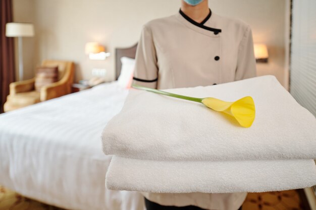 Image recadrée d'une jeune femme de chambre d'hôtel debout dans une suite avec une pile de serviettes fraîches et de calla lily