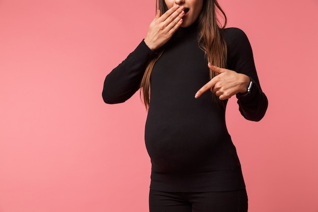 Photo image recadrée d'une jeune femme enceinte debout isolé sur rose, doigt pointé