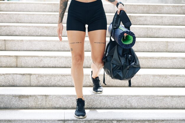 Image recadrée d'une jeune femme en forme en short de sport descendant les escaliers avec un sac de sport dans les mains