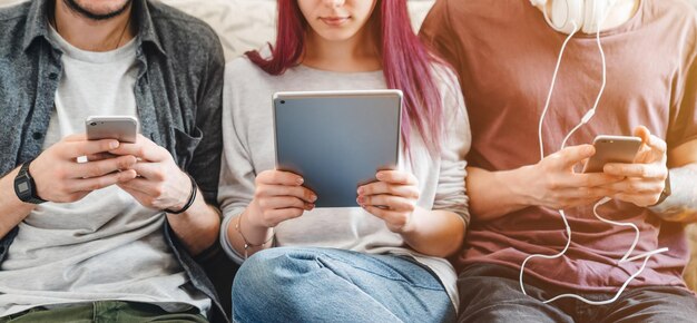 Image recadrée de jeunes avec des gadgets assis sur un canapé à l'intérieur