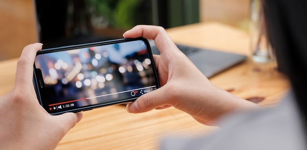 Image recadrée d'une main féminine tenant un smartphone et regardant une vidéo en se tenant debout à l'extérieur.