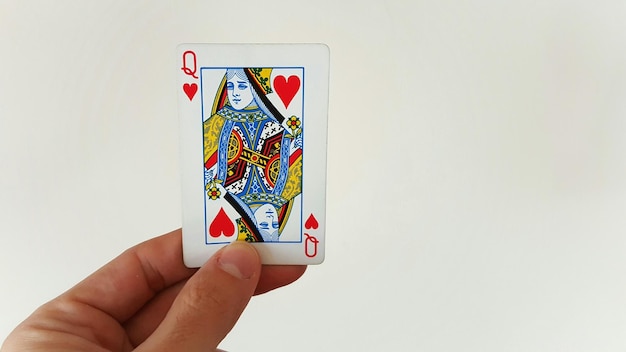 Image recadrée de la main tenant la reine de cœurs contre le mur blanc