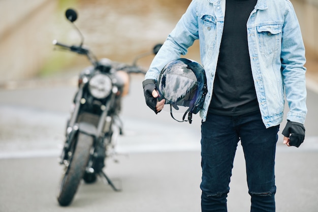 Image recadrée d'un motocycliste debout avec un casque dans les mains