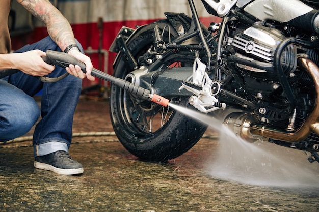 Image recadrée d'un motocycliste lavant son vélo dans un garage après un long trajet vers une autre ville