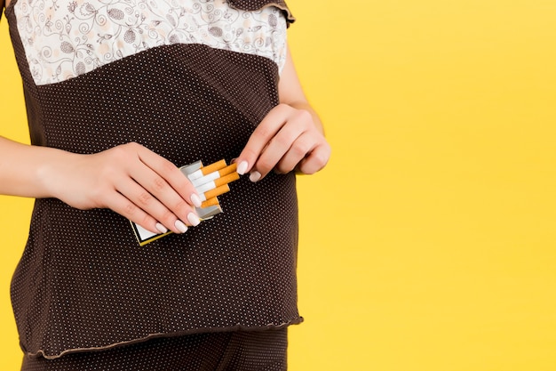 Image recadrée d'un paquet de cigarettes sur fond jaune. Mauvaise habitude d'une femme enceinte en pyjama marron. Mère insouciante.