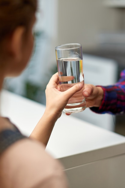 Image recadrée d'une petite fille tenant un verre d'eau dans la cuisine avec la mère.