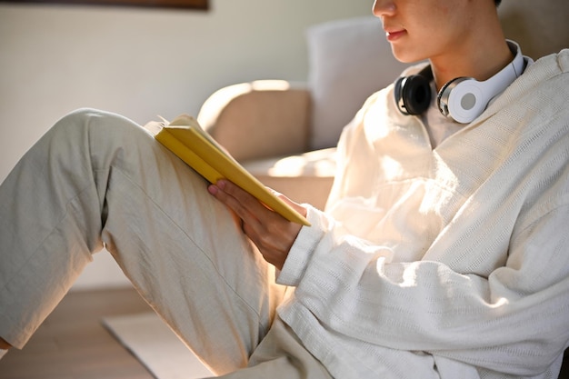 Image recadrée et vue de côté d'un jeune homme asiatique se concentrant sur la lecture d'un livre