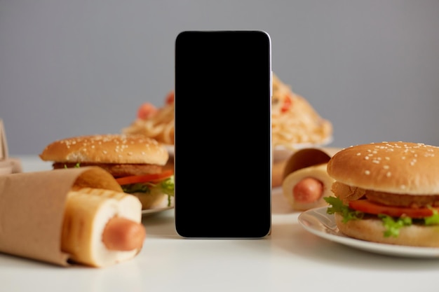 Image de restauration rapide sur table délicieuse saucisse dans la pâte pâtes et escalopes de viande hamburgers téléphone mobile avec zone de publicité de maquette d'affichage vide