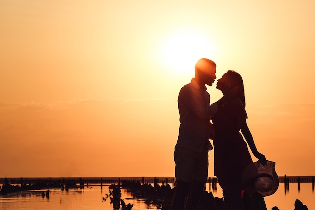 Image de la silhouette d'un couple aimant s'embrasser au coucher du soleil sur un lac