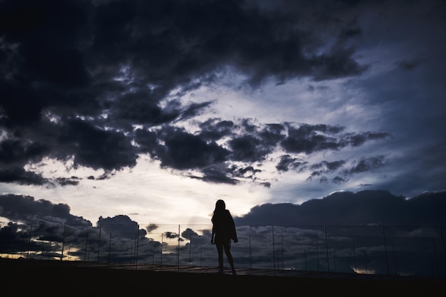 Image silhouette d'une femme debout seule avec un ciel nuageux au coucher du soleil