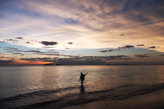 Image de silhouette d'une femme marchant dans la mer avant le coucher du soleil