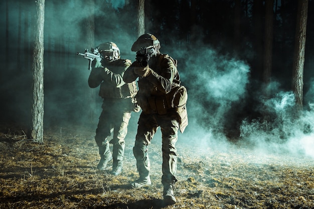 Image de soldats dans la fumée se déplaçant en opération de combat. Contre-jour, nuit noire, forêt