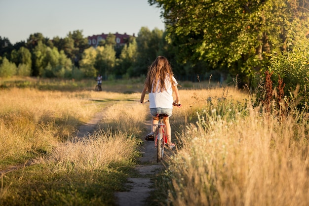 Image tonique de belle fille faisant du vélo dans les champs au coucher du soleil