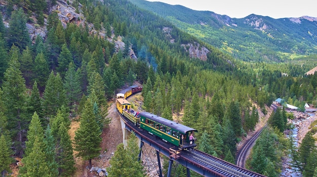 Image d'un train de locomotive avec des passagers traversant des pins en montagne